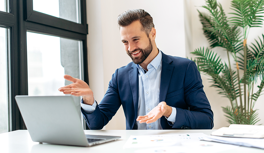 man in suit is smiling and watching something on his laptop in the office