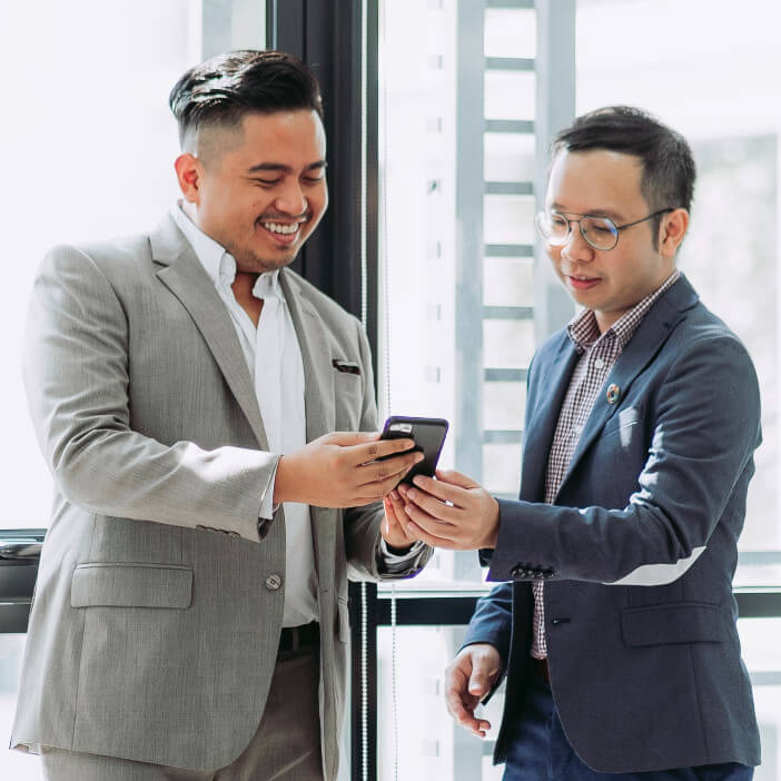 businessmen are looking at something on a phone